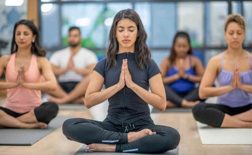 group of students attending yoga class sitting in lotus pose